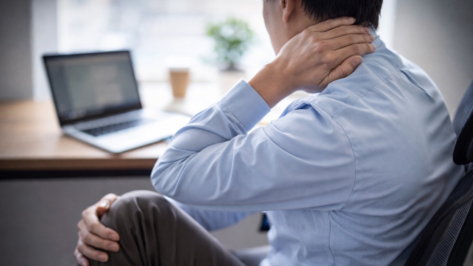 一名上班族坐在辦公椅上進行頸部伸展，桌上可見筆電與咖啡，呈現久坐工作後進行放鬆伸展的情境。